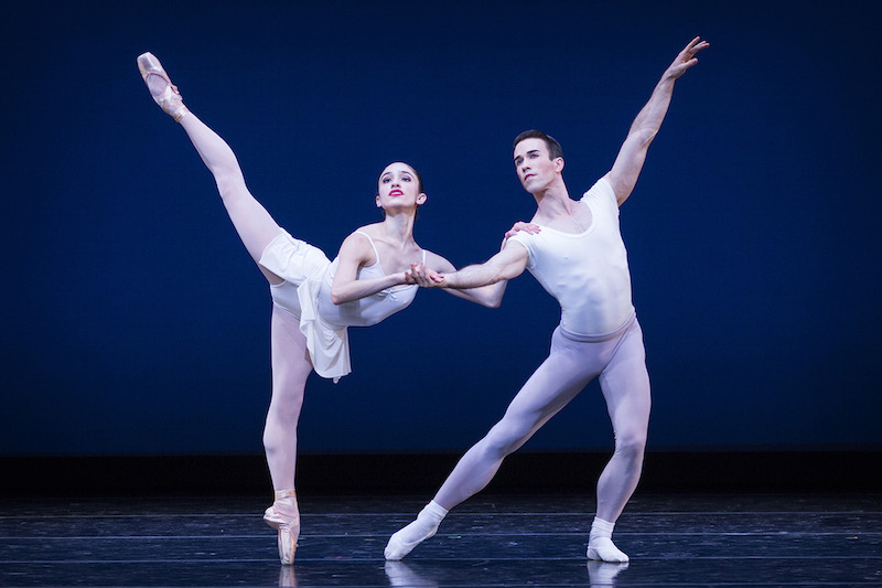 A woman en pointe leans on her male partner, who is in a lunge, and raises her leg high behind her in an arabesque